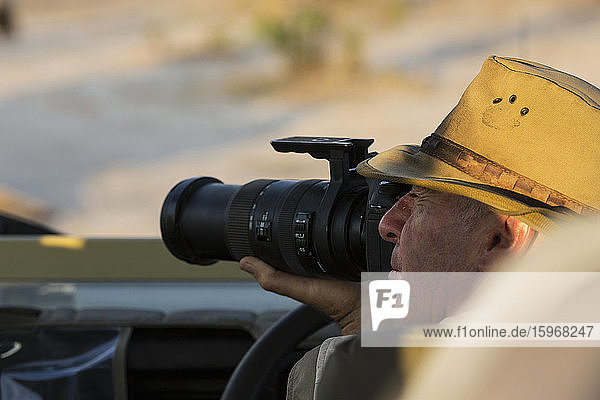 Ein Mann mit einem Buschhut  der eine Kamera mit langer Linse benutzt.