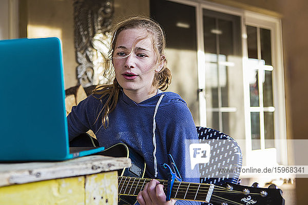 A teenage girl looking at laptop  singing and playing guitar