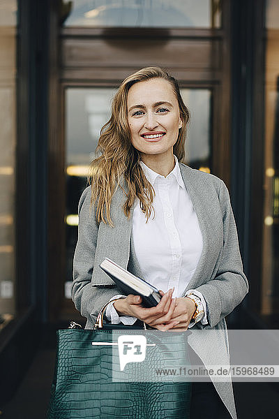 Porträt einer lächelnden Geschäftsfrau mit Buch und Tasche in einem Geschäft in der Stadt
