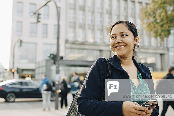 Lächelnde Unternehmerin mit stehendem Telefon in der Stadt