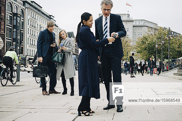 Unternehmer und Unternehmerinnen  die ein Smartphone benutzen  während sie in der Stadt auf der Straße stehen