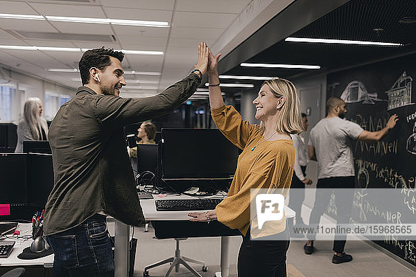 Male and female professional celebrating success while gesturing high-five at office desk