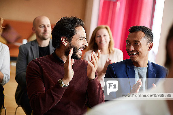Smiling male and female entrepreneurs clapping while attending office seminar