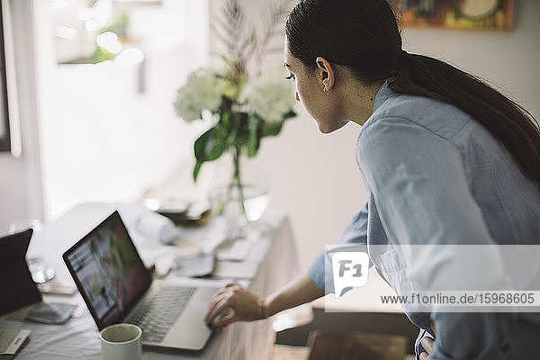 Seitenansicht einer Unternehmerin mit einem Laptop auf einem Tisch im Heimbüro