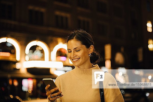 Lächelnde Frau  die nachts in der Stadt steht und per Handy SMS schreibt