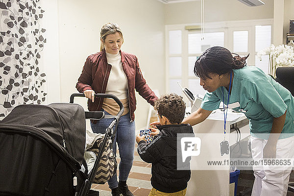 Kinderarzt gibt Aufkleber an Junge  während Mutter mit Kinderwagen im Krankenhaus steht