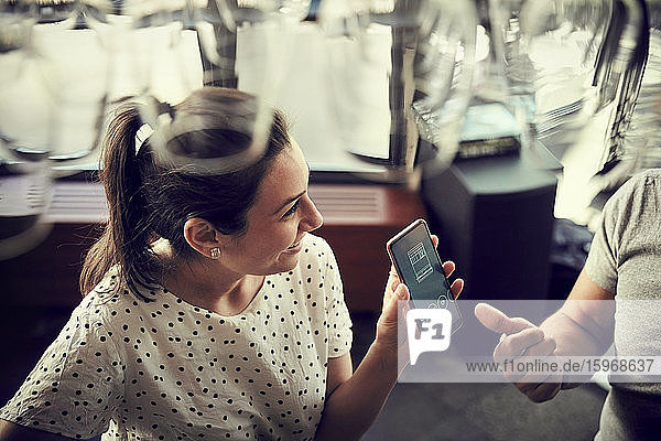 Hochwinkelansicht einer lächelnden Frau  die ihrem männlichen Partner im Cafe ein Smartphone zeigt