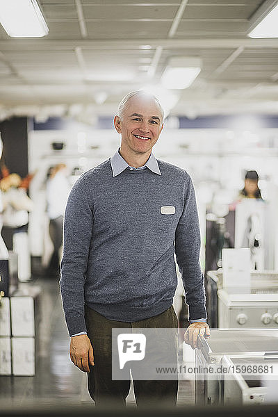 Portrait of smiling mature salesman standing in electronics store