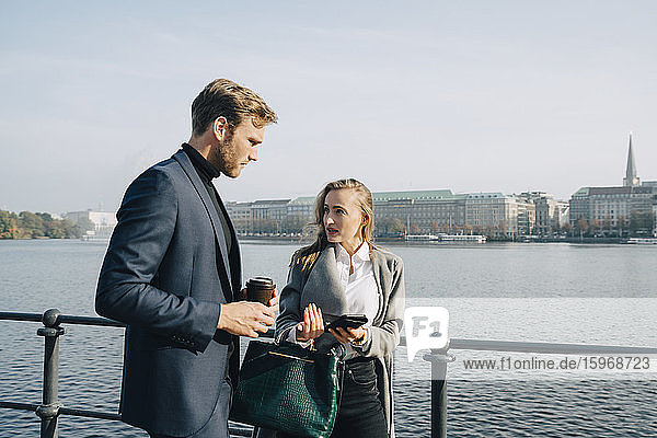 Side view of entrepreneur talking to coworker while standing against sea during sunny day
