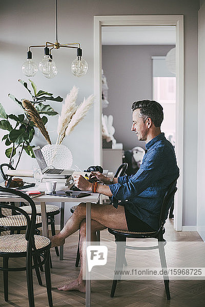 Mann sitzt am Tisch und arbeitet von zu Hause aus in Unterwäsche