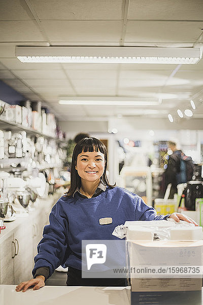 Porträt einer lächelnden Verkäuferin mit Gerät stehend im Elektronikladen