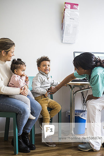 Weibliche Ärztin untersucht den Magen des Jungen  während die Mutter mit der Tochter in der Klinik sitzt