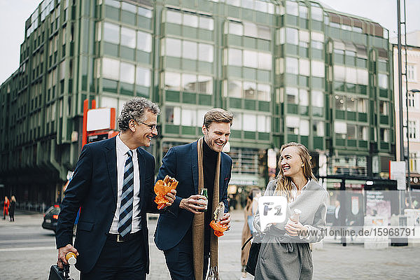 Smiling business professionals talking while holding food and drink in city