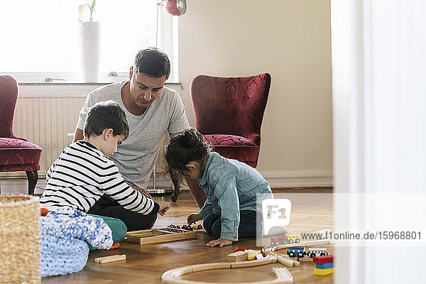 Vater sitzt  während Kinder zu Hause im Wohnzimmer spielen