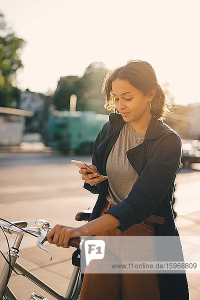 Junge Frau  die in der Stadt mit dem Fahrrad stehend im Netz surft