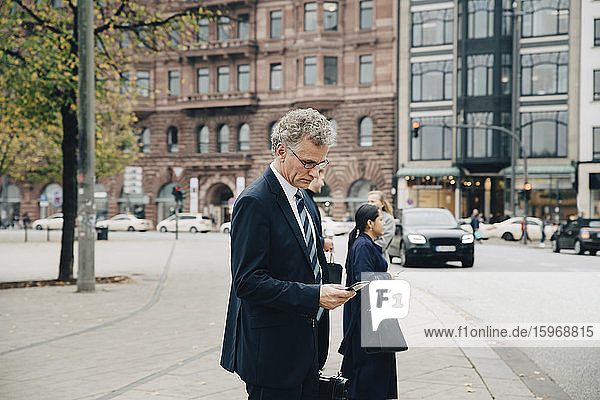 Side view of mature businessman using smart phone while standing in city