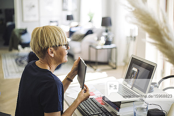 Frau  die zu Hause arbeitet und ihrem Kollegen einen digitalen Bildschirm zeigt