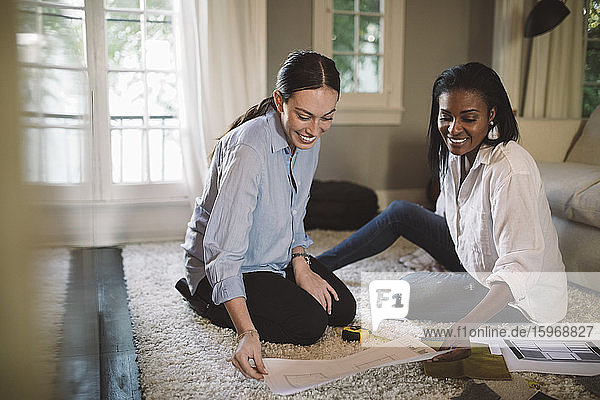 Smiling female designers discussing while sitting on carpet at home office