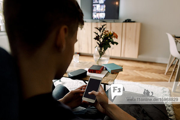 Teenager benutzt Smartphone  während er zu Hause auf dem Sofa sitzt