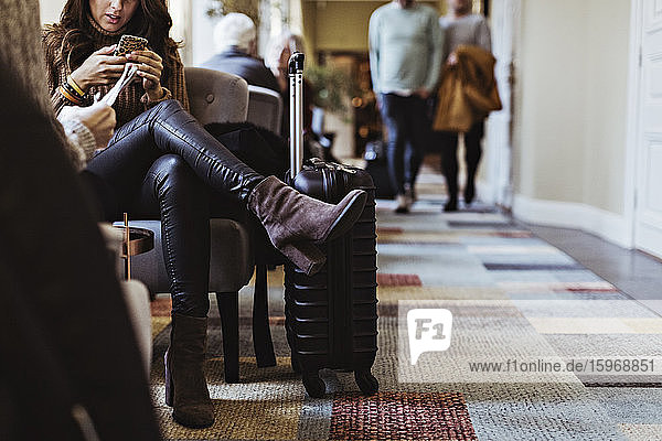 Unterer Teil einer mittelgroßen erwachsenen Frau  die ein Mobiltelefon benutzt  während sie auf einem Stuhl in der Hotellobby sitzt