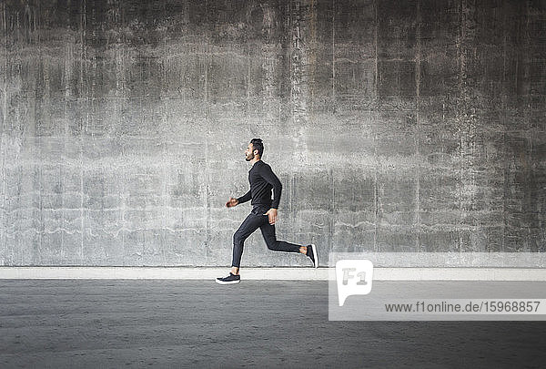 Side view of young man running by gray wall
