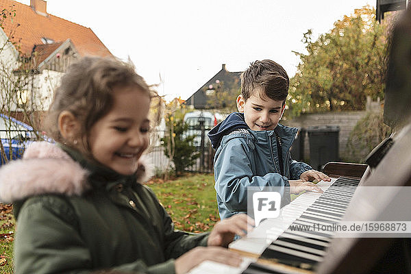 Lächelndes Mädchen spielt Klavier mit Bruder im Hinterhof