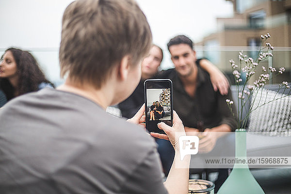 Rückansicht einer Frau  die während einer Terrassenparty Freunde per Smartphone fotografiert