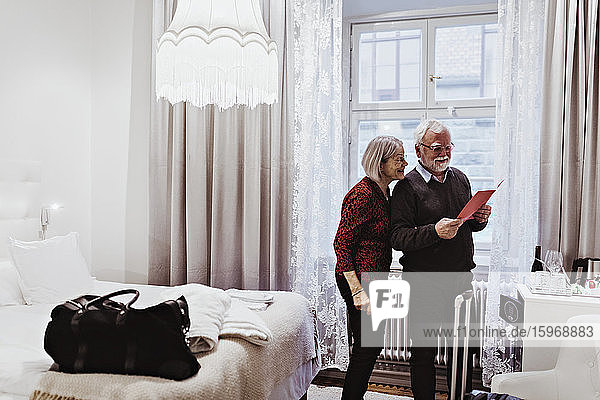Smiling senior couple reading card while standing in hotel room