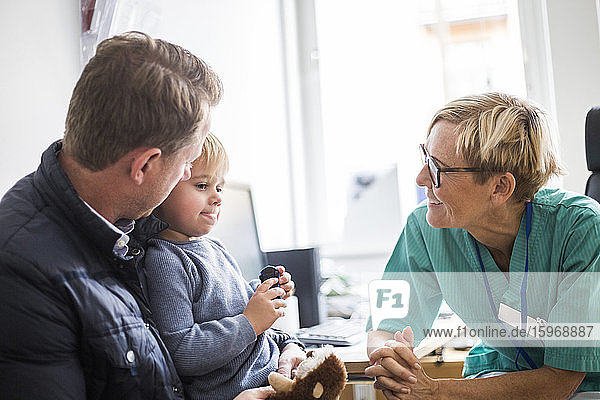 Lächelnder  reifer Arzt im Gespräch mit einem Jungen  dessen Vater in der Klinik ist
