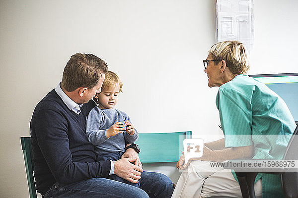 Seitenansicht einer reifen Ärztin  die mit einem Jungen spricht  dessen Vater in der Klinik ist