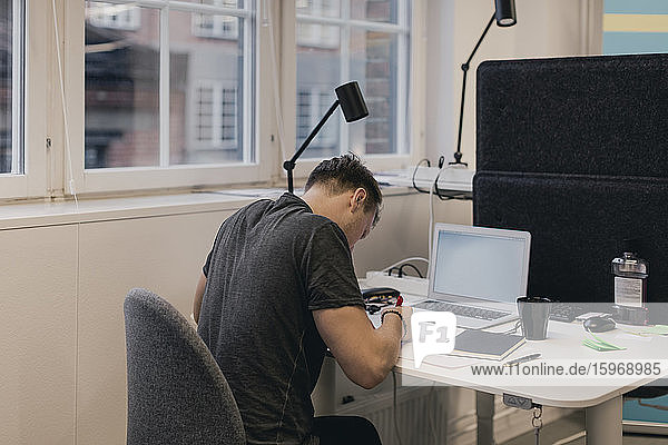 Businessman writing while using laptop at desk in creative office