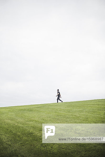 Seitenansicht eines jungen Mannes  der auf einem Grasfeld vor bewölktem Himmel geht