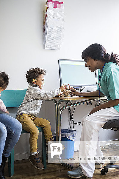 Junge spricht mit lächelnder Krankenschwester  während er in der Klinik mit einem Stofftier spielt