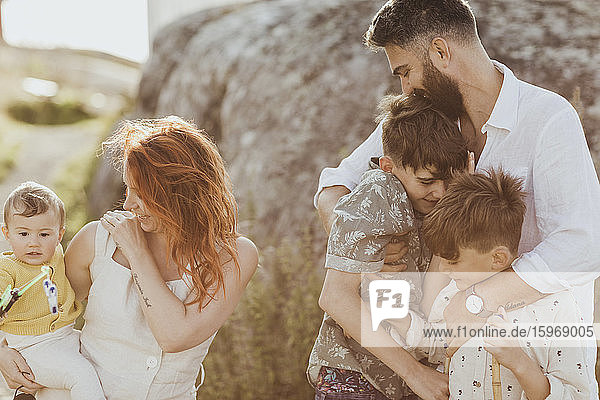 Lächelnder Vater umarmt Söhne  während die Mutter das Mädchen vor einer Felsformation betrachtet