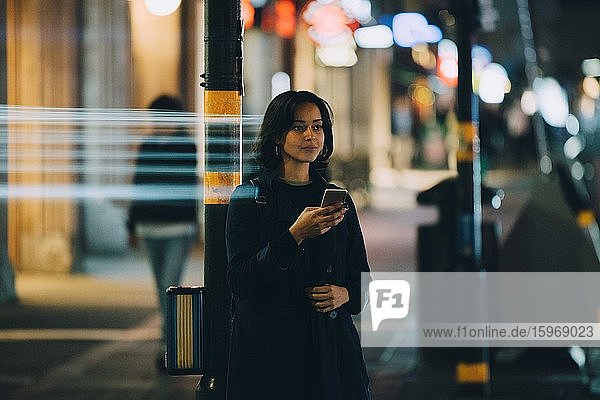 Young woman looking away while using mobile phone in city at night