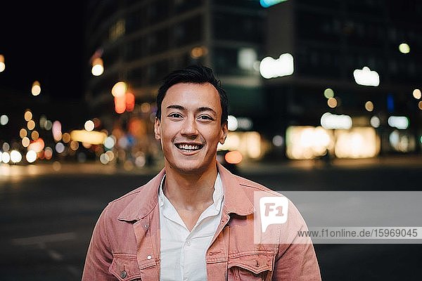 Portrait of smiling fashionable man standing in city at night