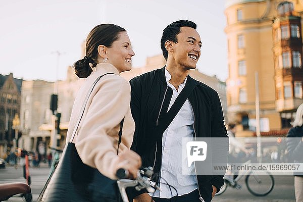 Lächelnde junge Frau mit Fahrrad schaut weg  während sie in der Stadt bei einem männlichen Freund steht
