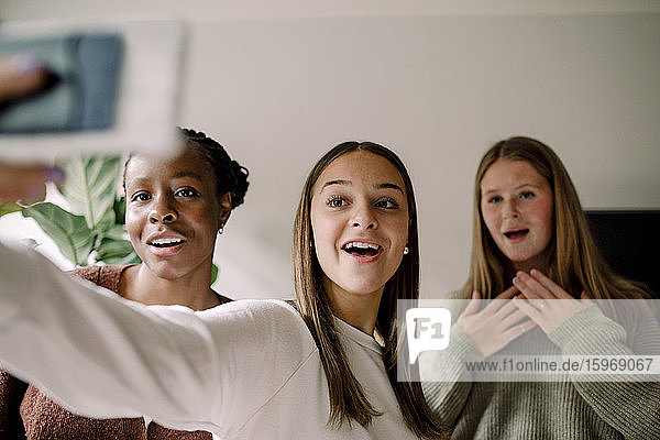 Lächelnde Mädchen im Teenageralter  die sich zu Hause mit dem Handy selbstständig machen