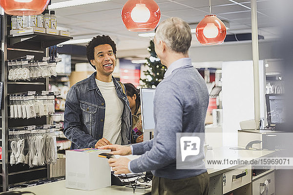 Smiling male customer with kettle box talking to mature owner while standing in electronics store
