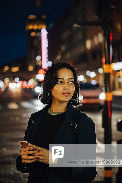 Junge Frau schaut weg  während sie nachts in der Stadt telefoniert