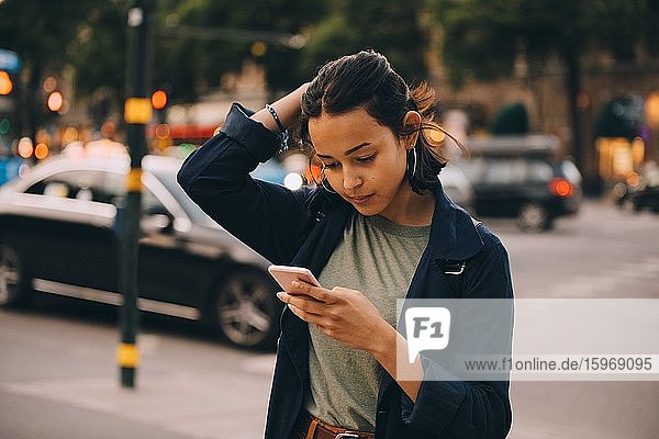 Texting Through Phone Young woman with hand in hair texting through phone while standing on ...