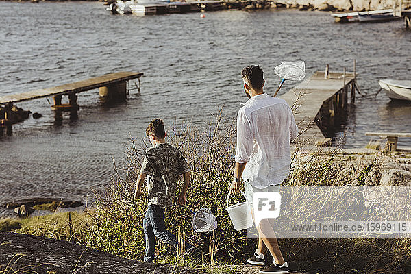 Rückansicht von Vater und Sohn  die am Wochenende mit einem Fischernetz auf dem Meer spazieren