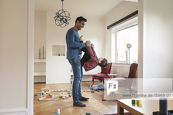 Smiling father lifting playful son while standing in living room