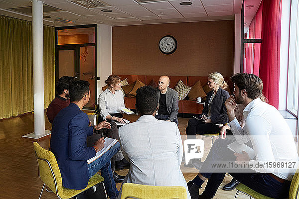 Male and female entrepreneurs discussing while sitting in circle during office workshop