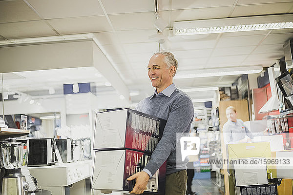 Smiling mature salesman with boxes walking in electronics store