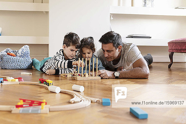 Kinder spielen mit dem Spielzeugblock  während sie mit dem Vater auf dem Hartholzboden liegen