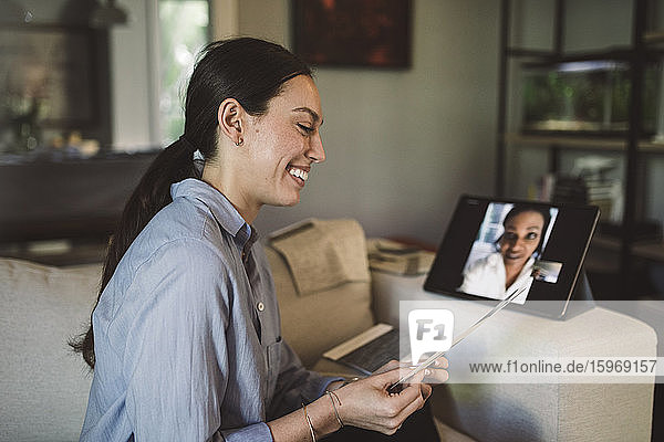 Smiling female entrepreneur with fabric swatch talking through laptop on video conference while working at home
