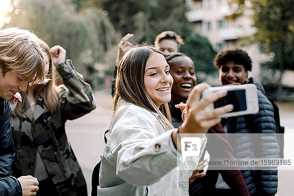 Happy multi-ethnic friends taking selfie with mobile phone on street in city