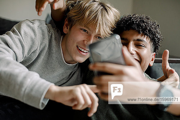Lächelnde Teenager  die sich zu Hause mit einem Smartphone selbstständig machen