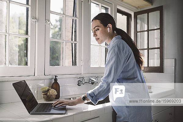 Seitenansicht einer weiblichen Fachkraft  die einen Laptop auf der Theke im Heimbüro benutzt